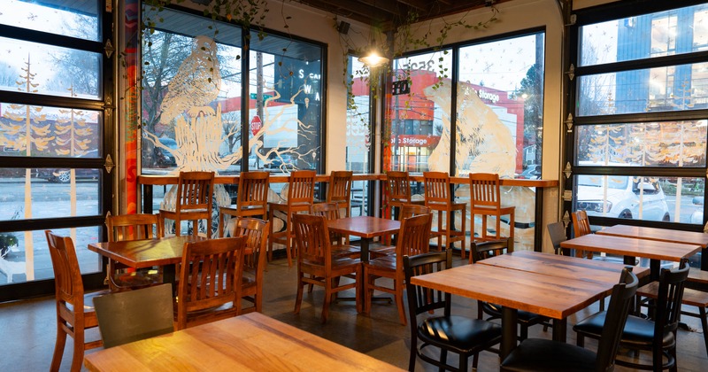 Interior of a café with wooden tables, chairs, and large decorated windows
