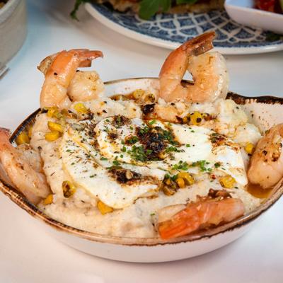 Shrimp and corn grits bowl topped with a fried egg and herbs.