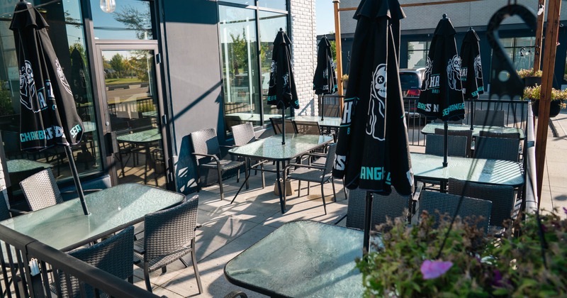 Sunlit restaurant patio with glass tables, woven chairs, closed black branded umbrellas