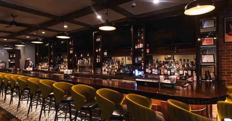A modern bar interior with a long wooden counter, mustard colored chairs