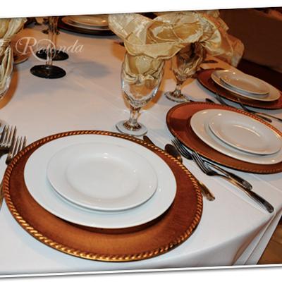 Formal table setting featuring white plates on copper chargers with gold napkins.