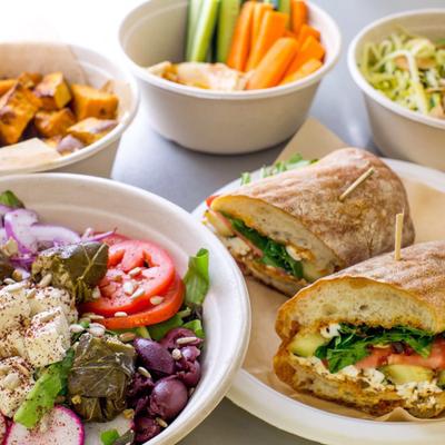 Bowl of salad served alongside sandwich, sides and condiments.