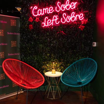 Two colorful chairs against a leafy backdrop with a pink neon sign.