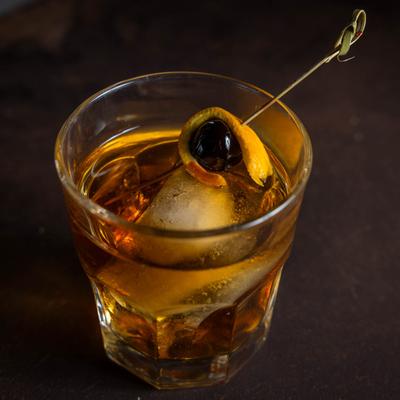 A glass of Old Fashioned garnished with cherry and lemon peel, close up.