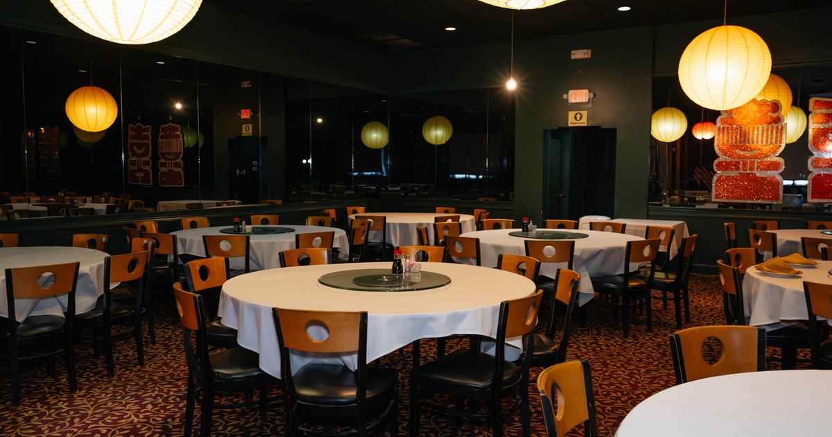 Interior of a restaurant with round tables, white tablecloths, and large yellow paper lanterns