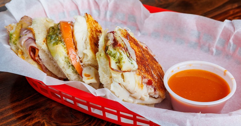 Grilled sandwiches with tomato and pesto served in basket with dipping sauce
