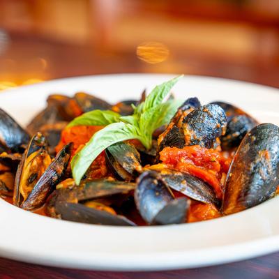 Mussels in marinara sauce, garnished with basil leaves, close up.