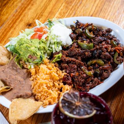 Marinated steak, with salad, guacamole, sour cream, rice, and refried beans.