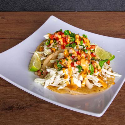 Fish tacos with shredded cabbage, diced tomatoes, and sauce drizzle.