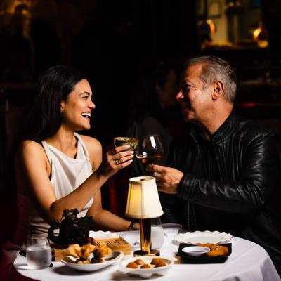 Couple seated at a round table toasting with glasses during dinner in a dimly lit dining room.