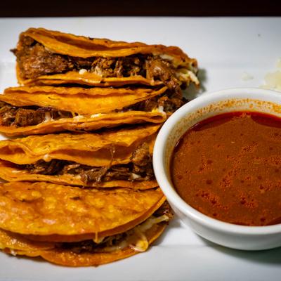 Birria tacos served with consommé on white plate.