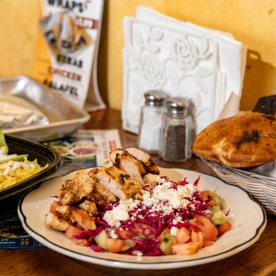 A colorful grilled chicken salad surrounded by a basket of pita, and salad dishes.