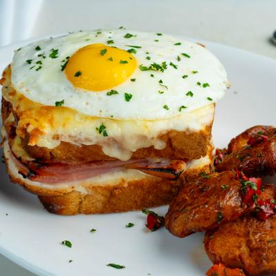 Sandwich - ham, melted cheese, a sunny-side-up egg, garnished with herbs, served with fried potato..