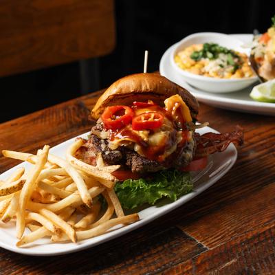 Cheeseburger with bacon and red peppers, served with fries on a plate.