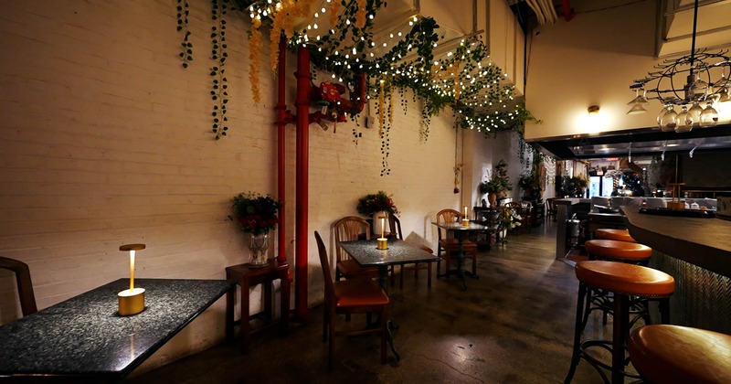 Interior of a cozy café with tables, chairs, foliage and warm lighting.