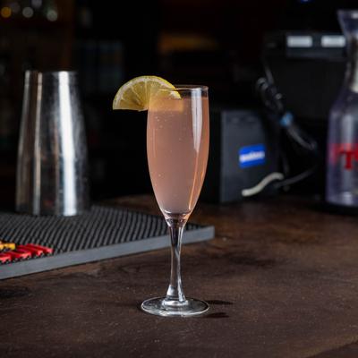 A translucent red vodka cocktail in a champagne glass, garnished with a lemon wedge.