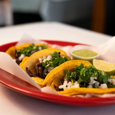 Three street tacos with lime wedge and green salsa.