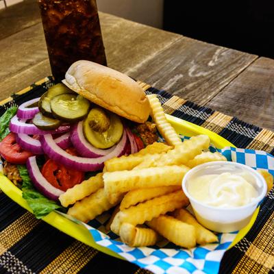 A pork tenderloin sandwich with fries and mayonnaise, accompanied with a soft drink.