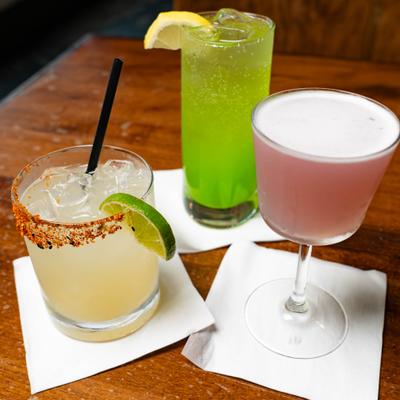 Three colorful cocktail placed on white napkins on a wooden table.
