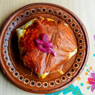 Large tortilla wrap topped with melted cheese, red sauce and pickled onion.