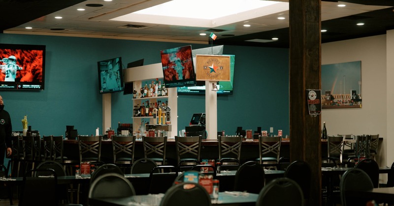 Interior of a bar and grill with a bar counter, tables, chairs, and televisions