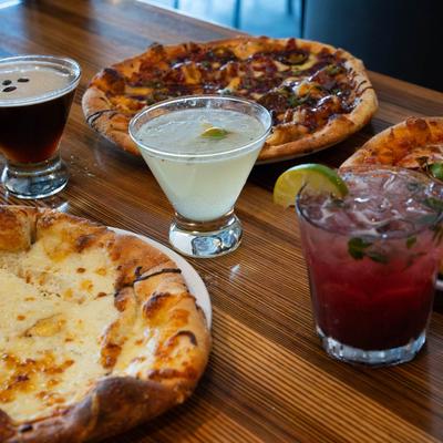 Assorted pizzas with cocktail drinks on a table.