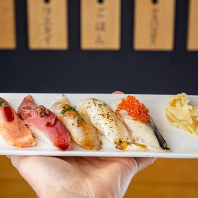 A hand holding a plate of assorted nigiri sushi rolls.