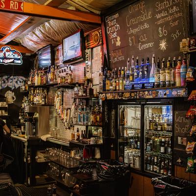 Bar area with blackboard, wall-mounted TVs, beer fridge, liquor bottles.