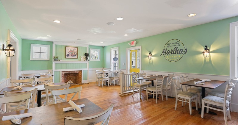 Bright, welcoming cafe interior with light green walls, wooden floors, and white, rustic furniture