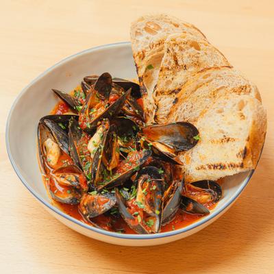 A bowl of spicy mussels served with grilled bread.