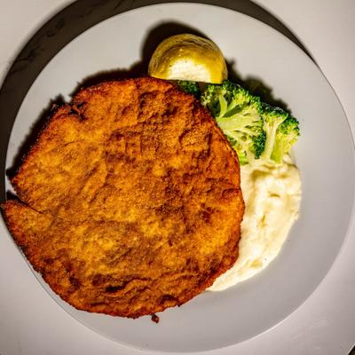 Breaded chicken breast served with mashed potatoes and broccoli.