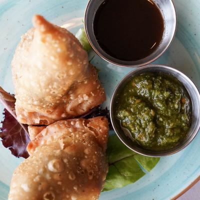 Fried samosas served with chutneys on a blue plate.