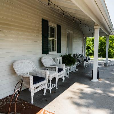 Front porch furnished with white wicker chairs and dark-trimmed windows.