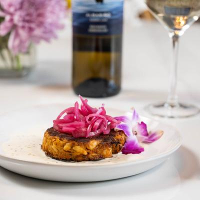 Crab cake with pickled red onion on top, garnished with flower.