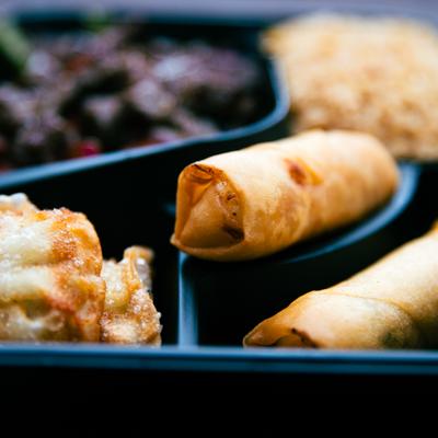 Spring rolls and fried dumplings in a takeout tray.