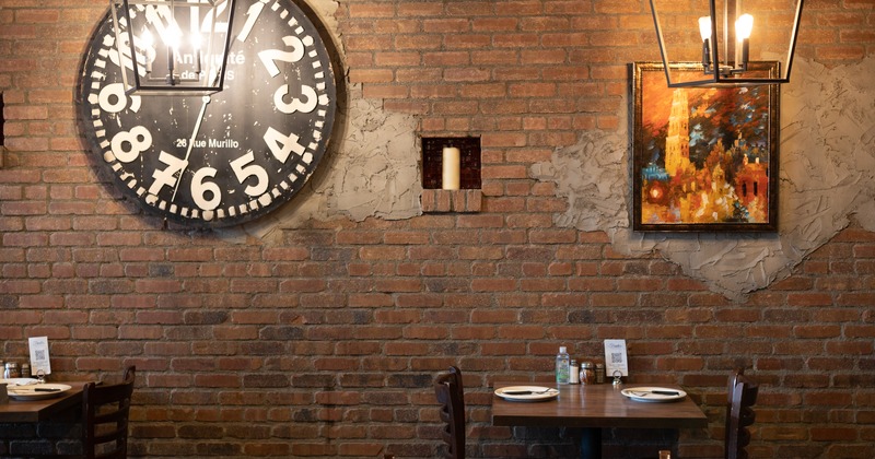 Interior, set dining tables by a brick wall, a large clock and a painting on the wall
