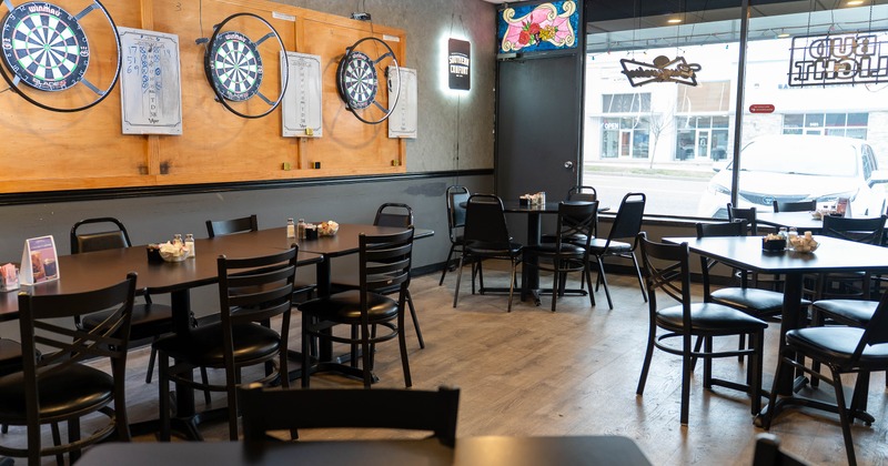 A casual dining area with dartboards on the wall and tables with black chairs.