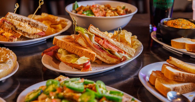 Assortment of sandwiches, chips, and dips on a dark table