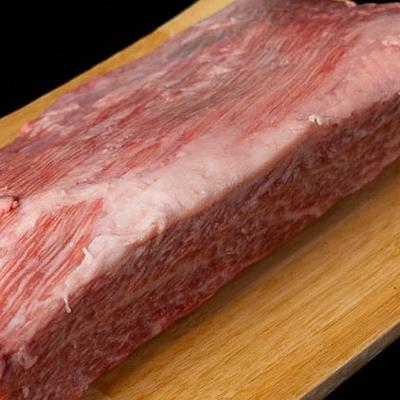 A slab of raw marbled meat rests on a wooden board against a black background.