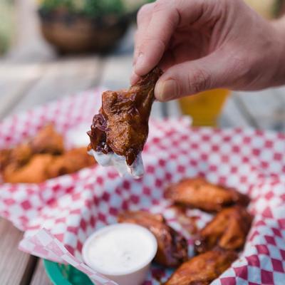Hand holding a chicken wing over a basket of wings and a cup of dipping sauce.