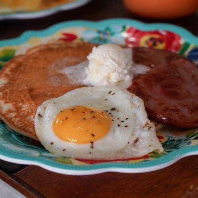 Pancakes topped with whipped butter, ham, and a fried egg.