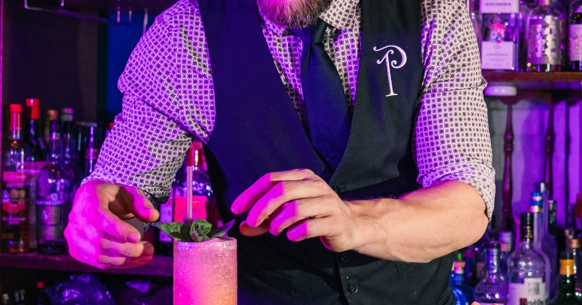 Bartender garnishes a cocktail with mint at a dimly lit bar.