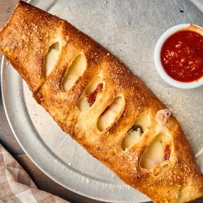 Stromboli served on a metal tray with a side of marinara sauce.
