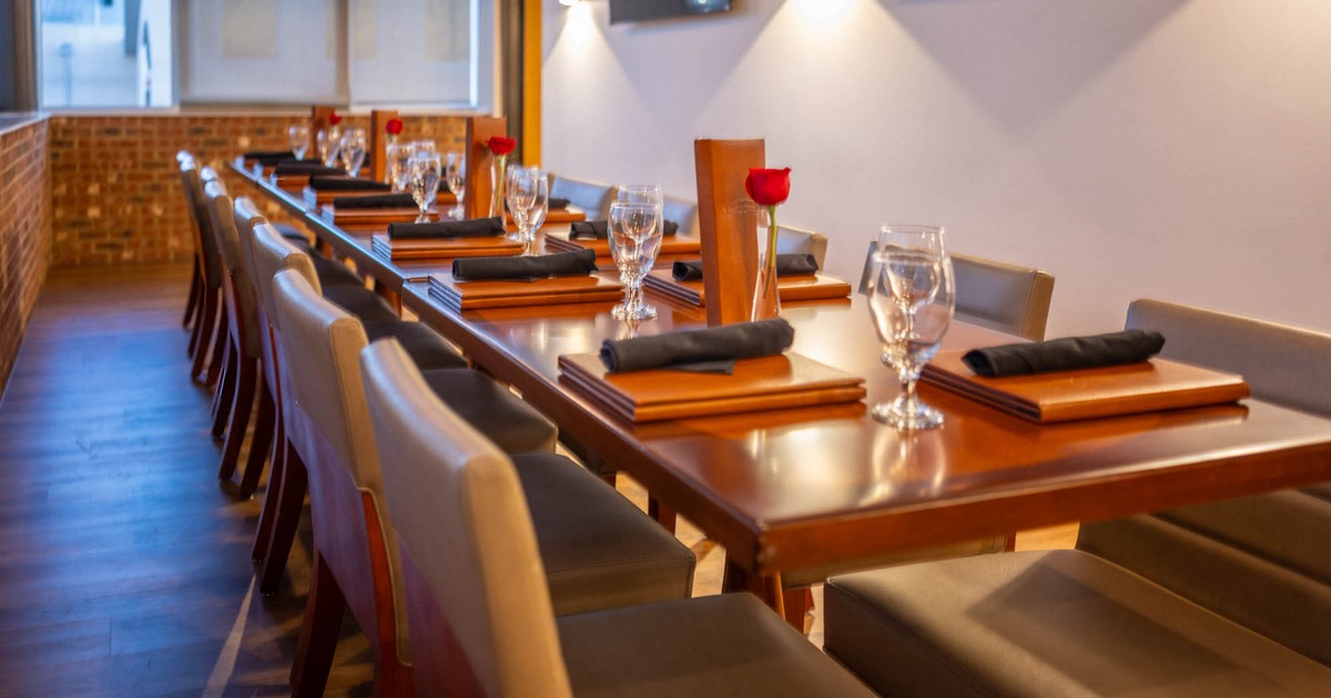 A line of conjoined tables with chairs, with place settings and flowers