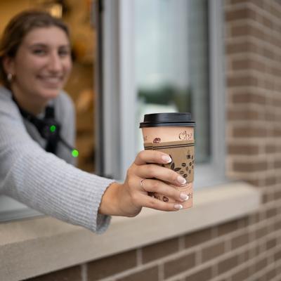 A smiling barista extends a coffee cup through a drive-thru window.
