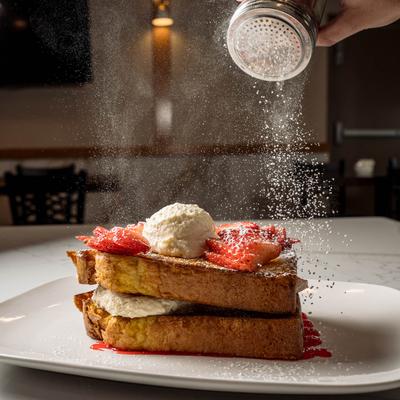 Powdered sugar being sprinkled over French toast with strawberries and cream.