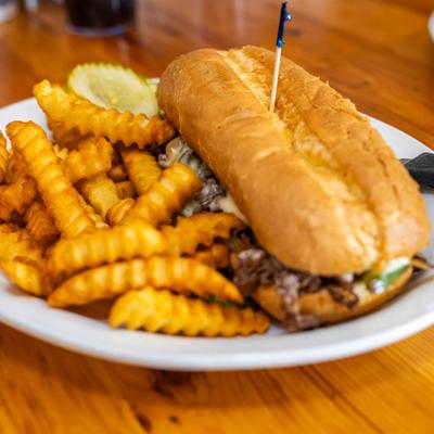 Philly cheesesteak sandwich with crinkle fries, served on a table.