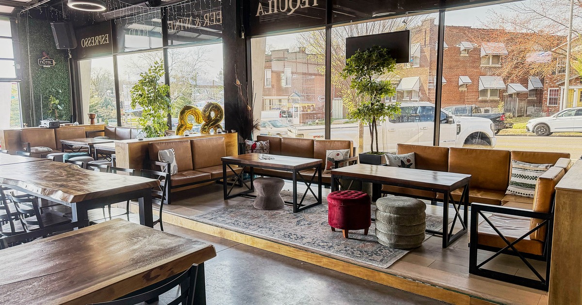 Interior of a café with large windows, wooden tables, leather benches, and visible street view