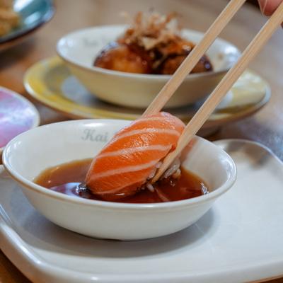 Salmon nigiri dipped in sauce with chopsticks.