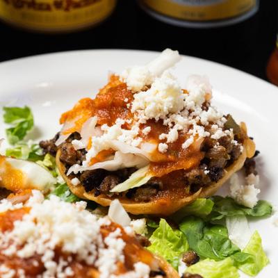 Stuffed tostada topped with sauce, cabbage and crumbled cheese.